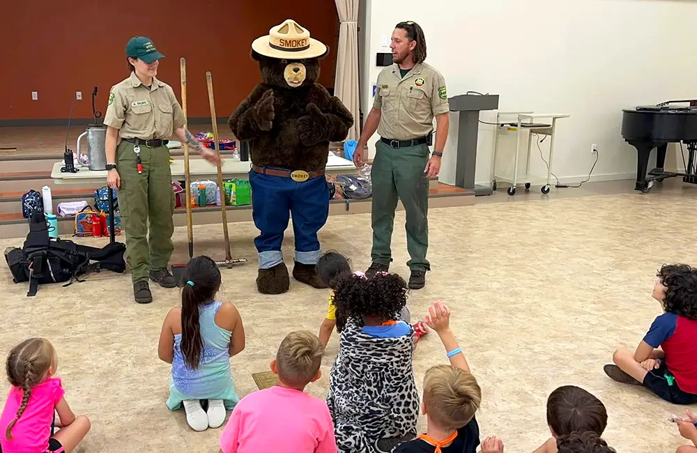 Forest Service rangers with Smokey Bear mascot presenting fire safety education to children